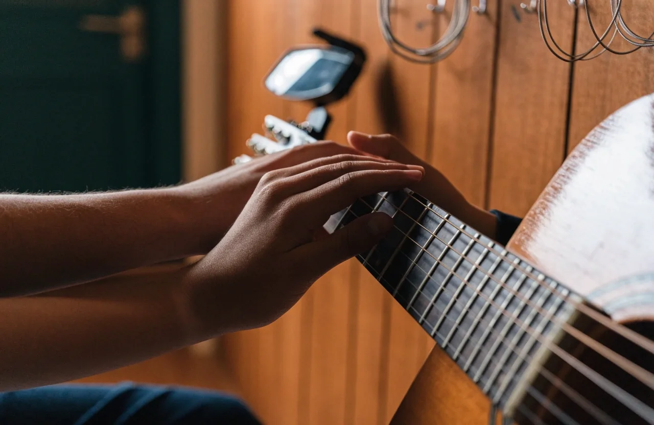 A tutor guiding a learner's fretting hand on a guitar neck