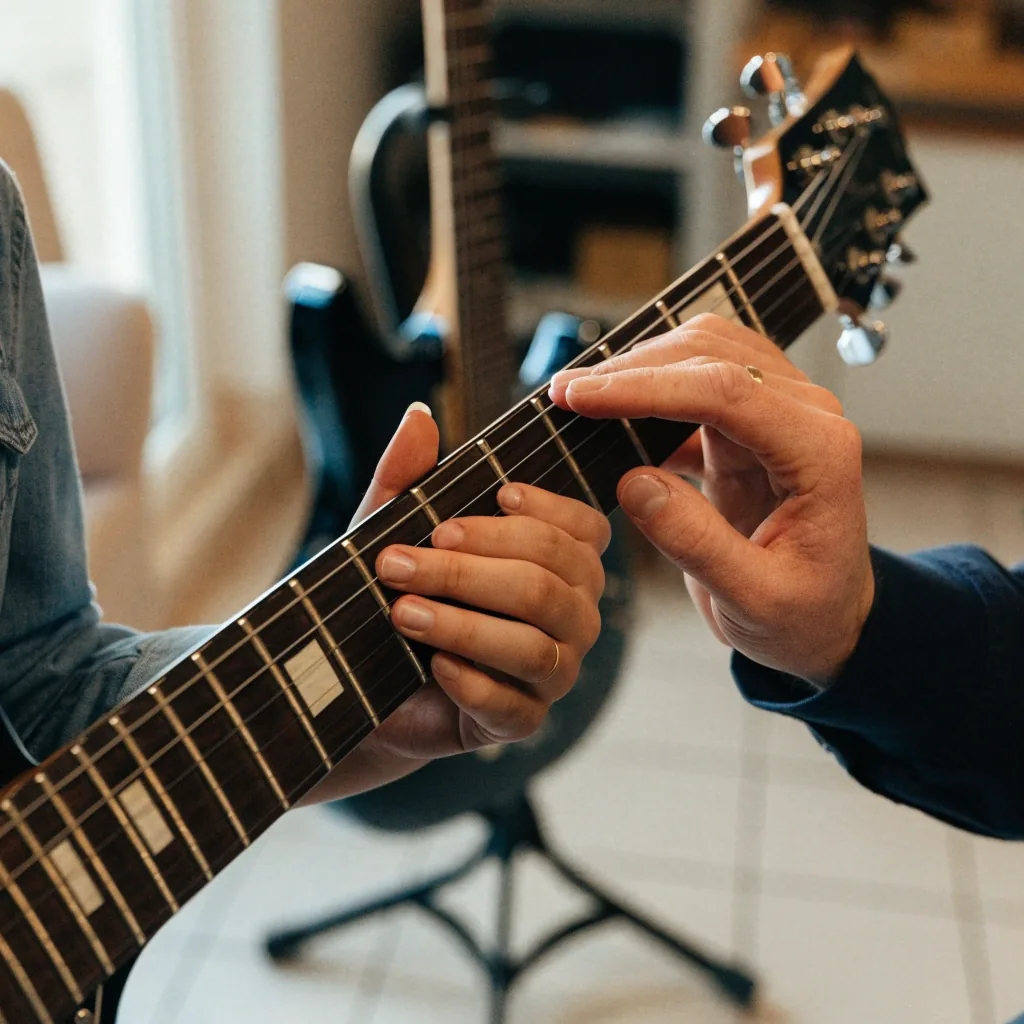 A tutor adjusting a student's fretting hand during a guitar lesson in a bright teaching room