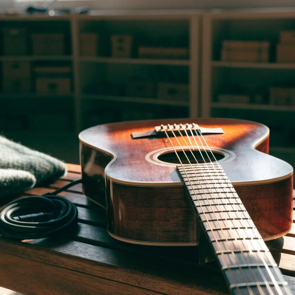 Acoustic guitar resting on a studio bench with a coiled cable in warm side light